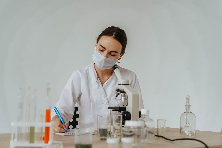 Lab worker analyzing samples with microscope, taking notes. Focus on science and safety.